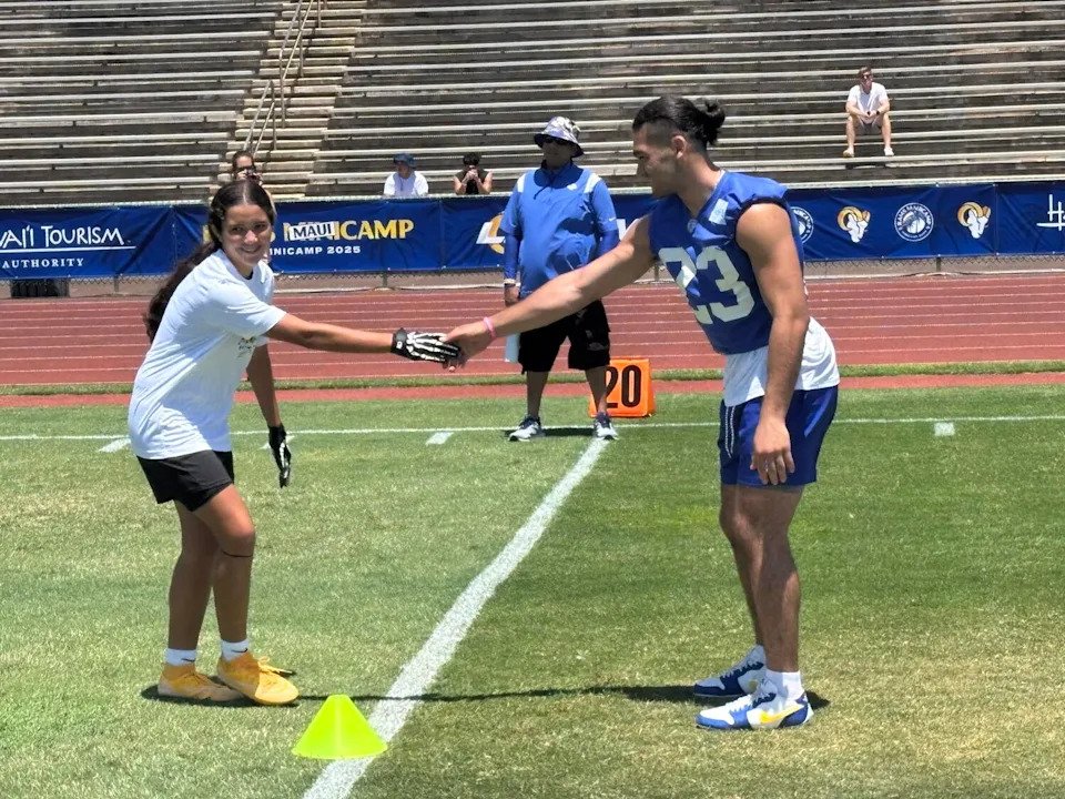 Rams wide receiver Puka Nacua shakes hands with a youth flag football player during a clinic drill.