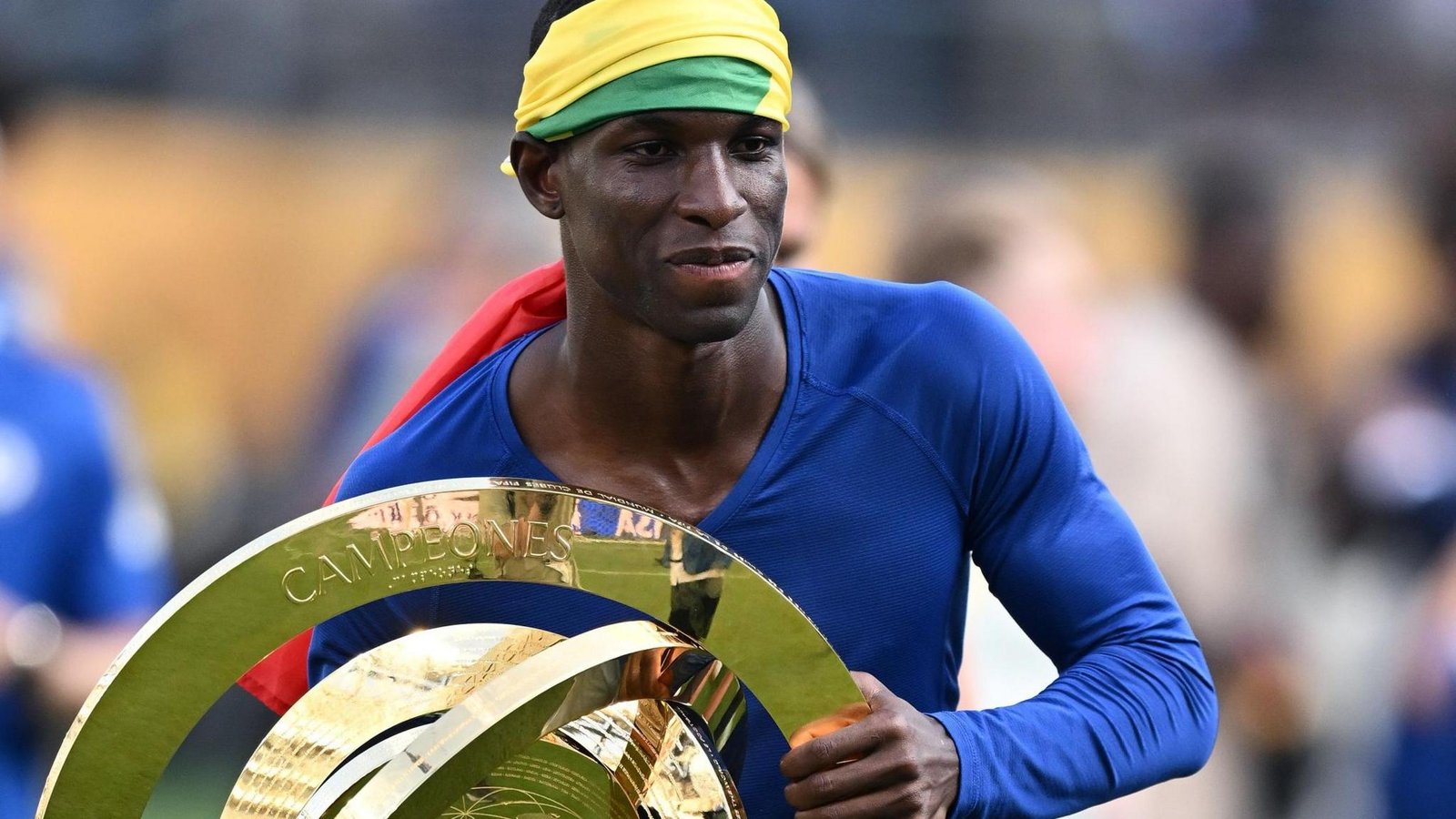Nicolas Jackson, wearing a blue long-sleeved undershirt and with a Senegalese flag wrapped around his head, holds the Club World Cup trophy