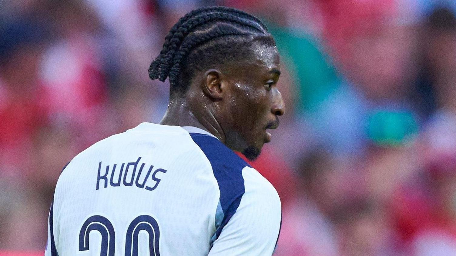 Mohammed Kudus with braided hair looks to his right as he is pictured from behind in a white Tottenham shirt with blue shoulder trim, with his name and half of his number 20 visible on the back of his kit