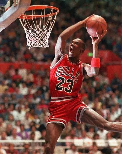 Michael Jordan wearing a Bulls basketball uniform and going up for a dunk