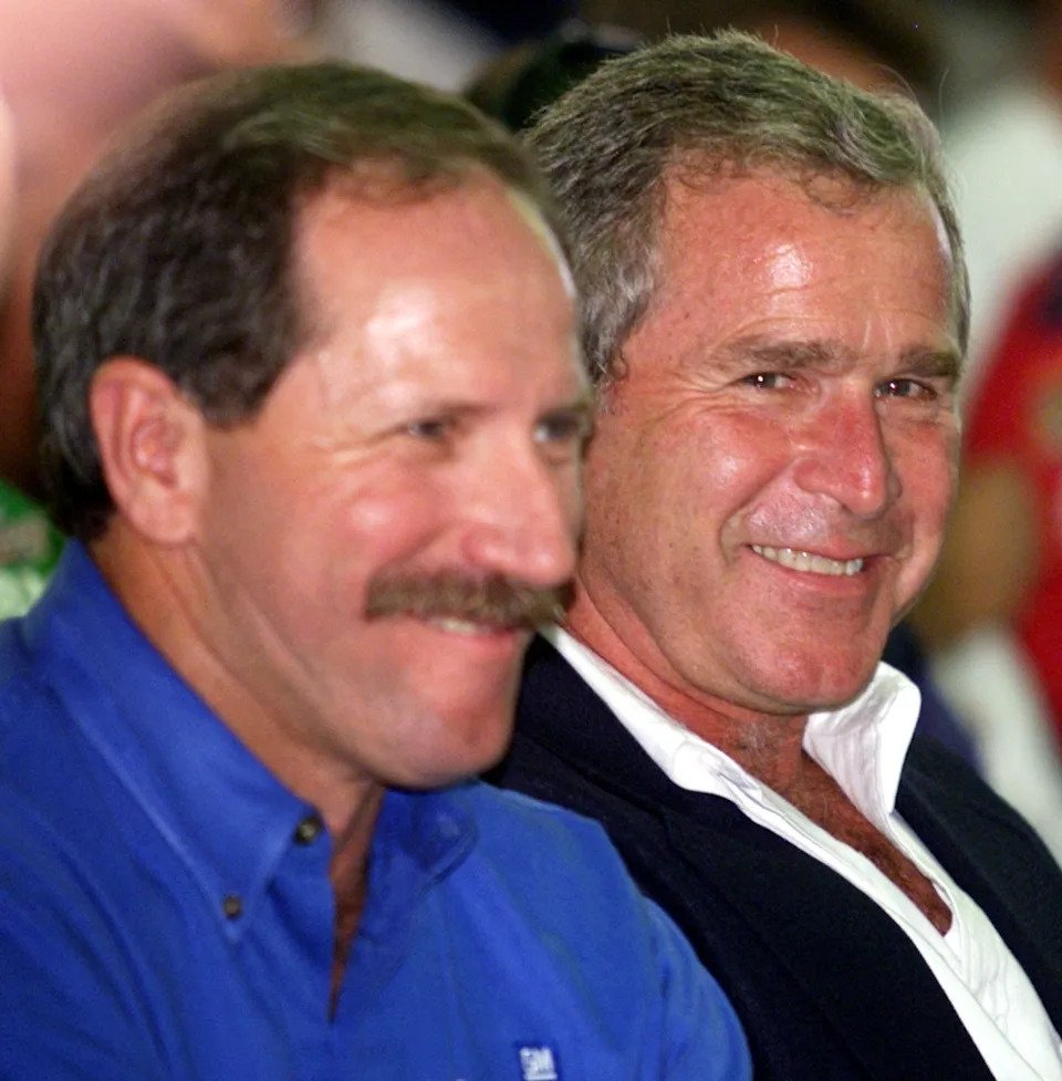 George W. Bush (R) shares a laugh with NASCAR driver Dale Earnhardt during a driver's meeting.