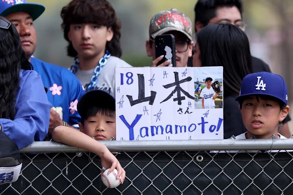 Fans hold a sign with pitcher Yoshinobu Yamamoto's name while waiting to seek autographs at Dodgers spring training.
