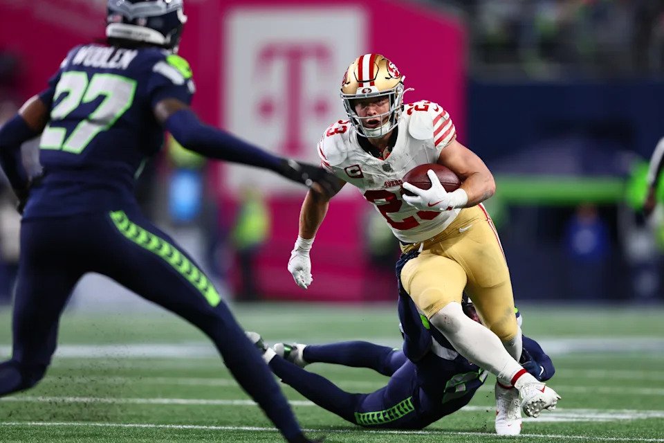 Jan 17, 2026; Seattle, WA, USA; San Francisco 49ers RB Christian McCaffrey (23) carries the ball as Seattle Seahawks CB Devon Witherspoon (21) defends during the first half in an NFC Divisional Round game at Lumen Field. Mandatory Credit: Kevin Ng-Imagn Images