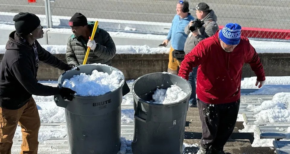 Workers move snow via trash cans at Bowman Gray Stadium.