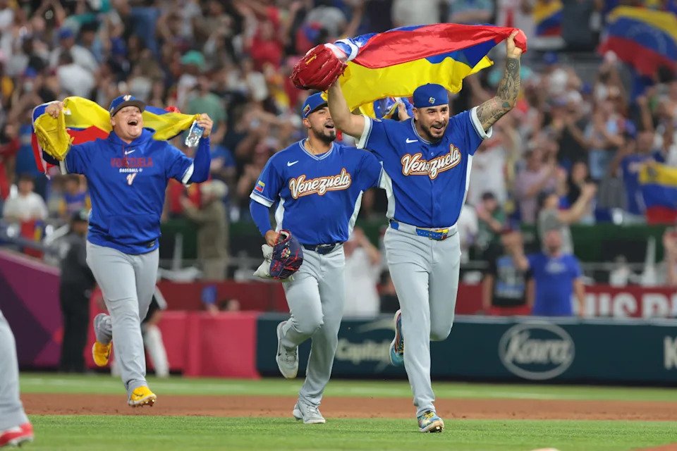 Venezuela pitcher José Buttó (70) celebrates with his country's flag after defeating Italy in a semifinal game of the 2026 World Baseball Classic.