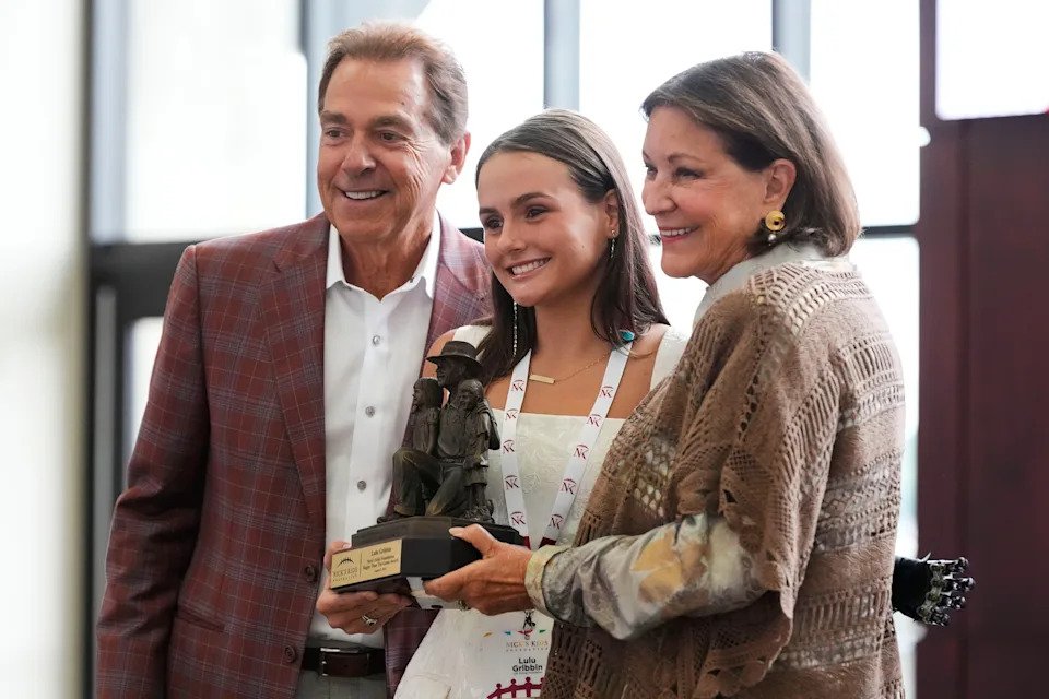 Lulu Gribbin, posing between Nick and Terry Saban, received the Greater Than The Game Award at Bryant-Denny Stadium in Tuscaloosa, Alabama in August 2025.