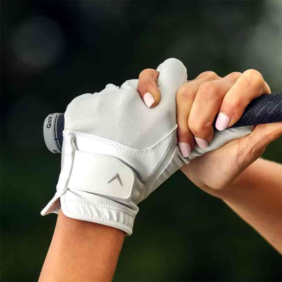 A close-up of two hands gripping a golf club—one in a white glove, the other with pale pink manicured nails—captures a special Mother's Day moment. The background is softly blurred, highlighting this intimate gesture.
