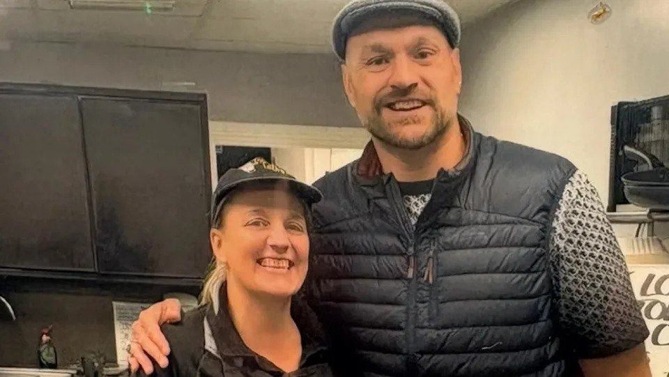 Rachel wears he Terry's Tato's uniform and stands next to Tyson who wears a farmer's cap and puffer gilet, they both smile brightly.