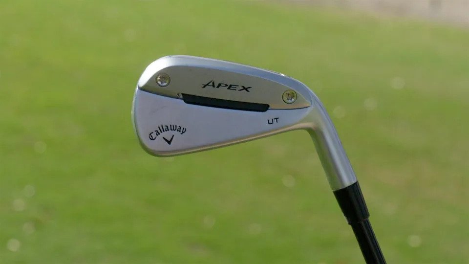 A close-up of a Callaway Apex UT golf club held outdoors, with a blurred green grass background.